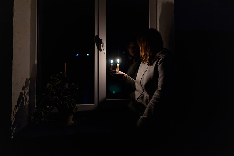 A woman holds a candle in a pitch black house looking out the window after a blackout knocked out her home's powerPicture